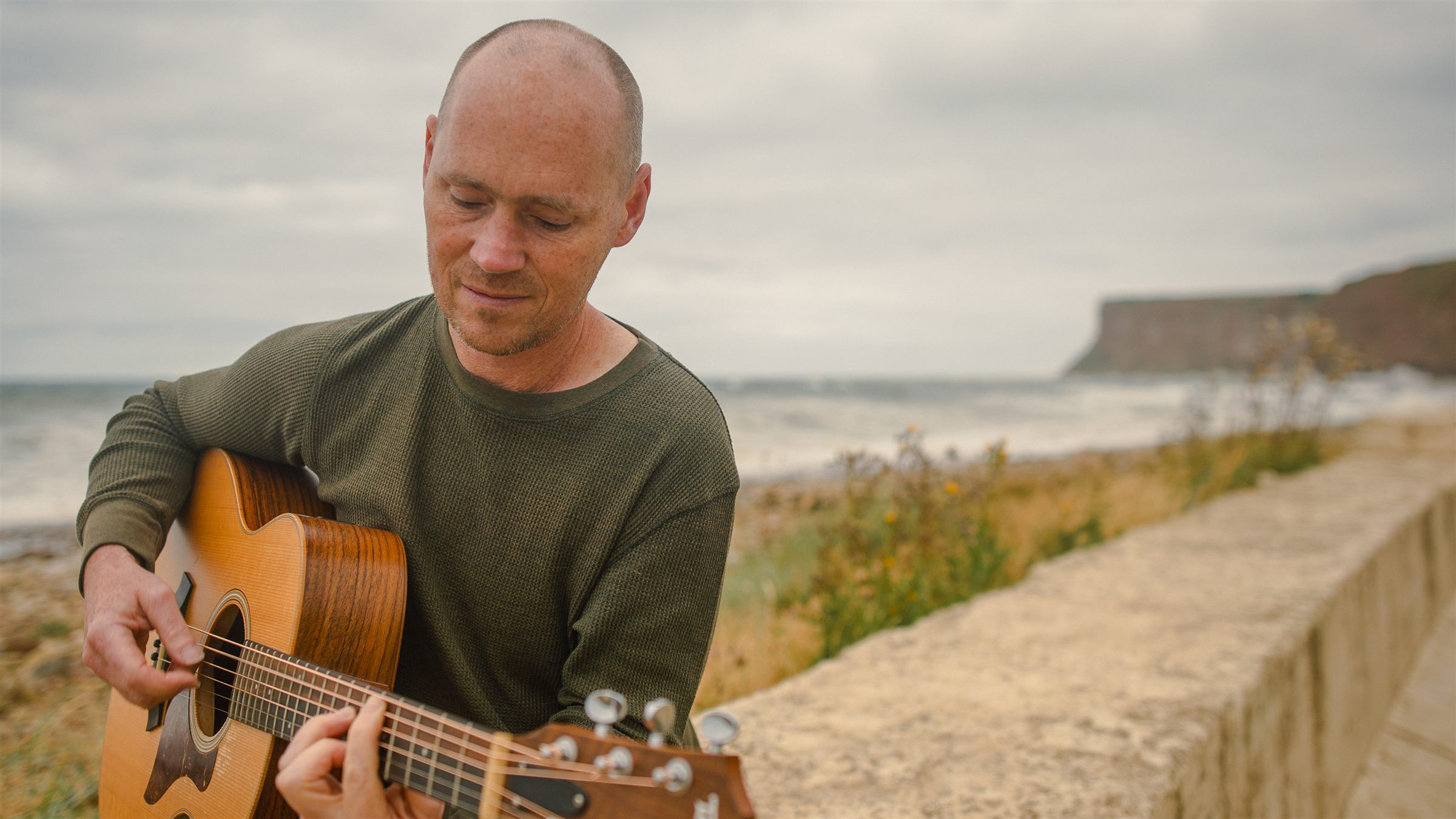 John Grummitt playing acoustic guitar by the sea